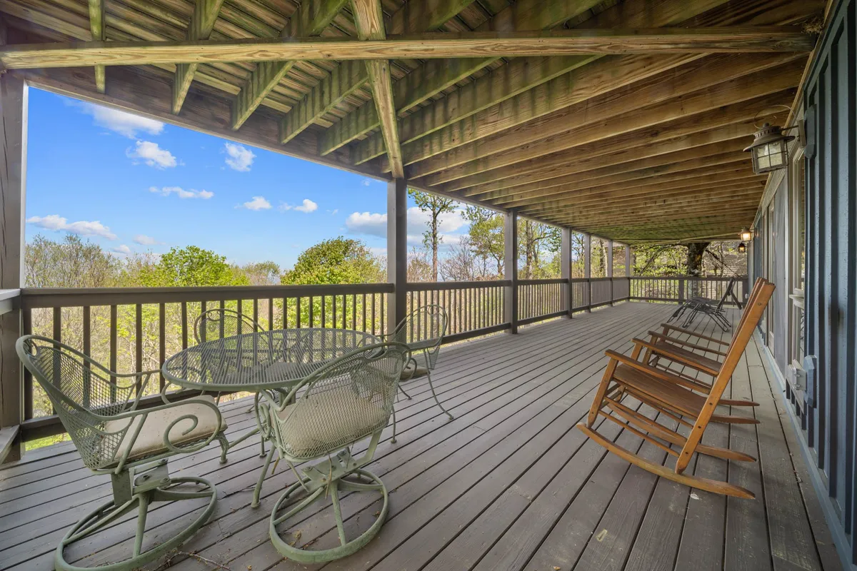 This image features a spacious outdoor porch area with wooden rocking chairs, a small table, and a wooden ceiling. The porch overlooks lush greenery and offers an inviting place to relax and enjoy the scenic mountain views. The setting is tranquil, perfect for unwinding with your pet after a day of adventure.