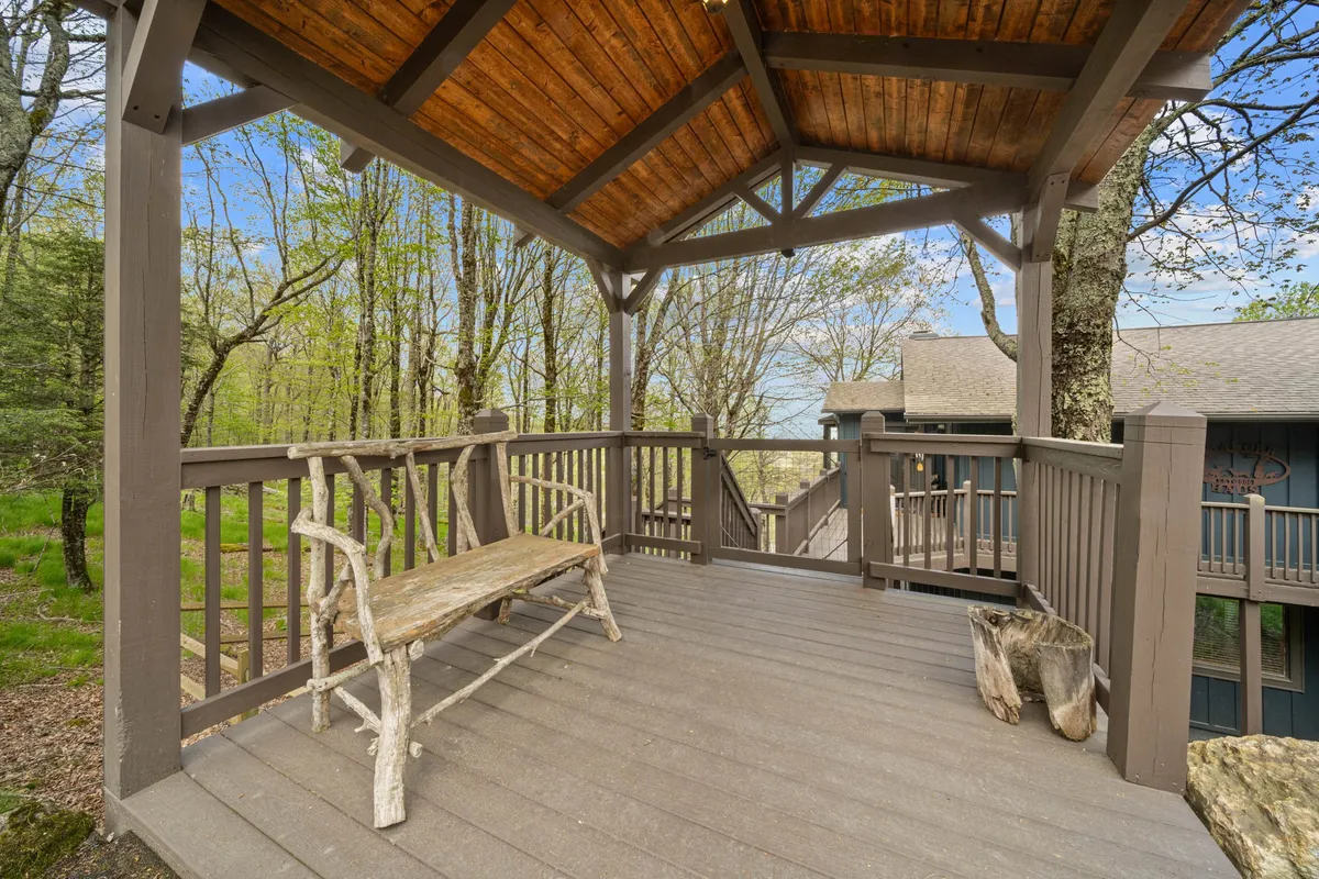 A rustic wooden bench sits under elegant ceiling beams, surrounded by lush trees. The outdoor area exudes a peaceful atmosphere, ideal for relaxing, reading, or gathering with friends. The scene suggests the perfect spot to watch the sunrise, host summer barbecues, or stargaze at night.