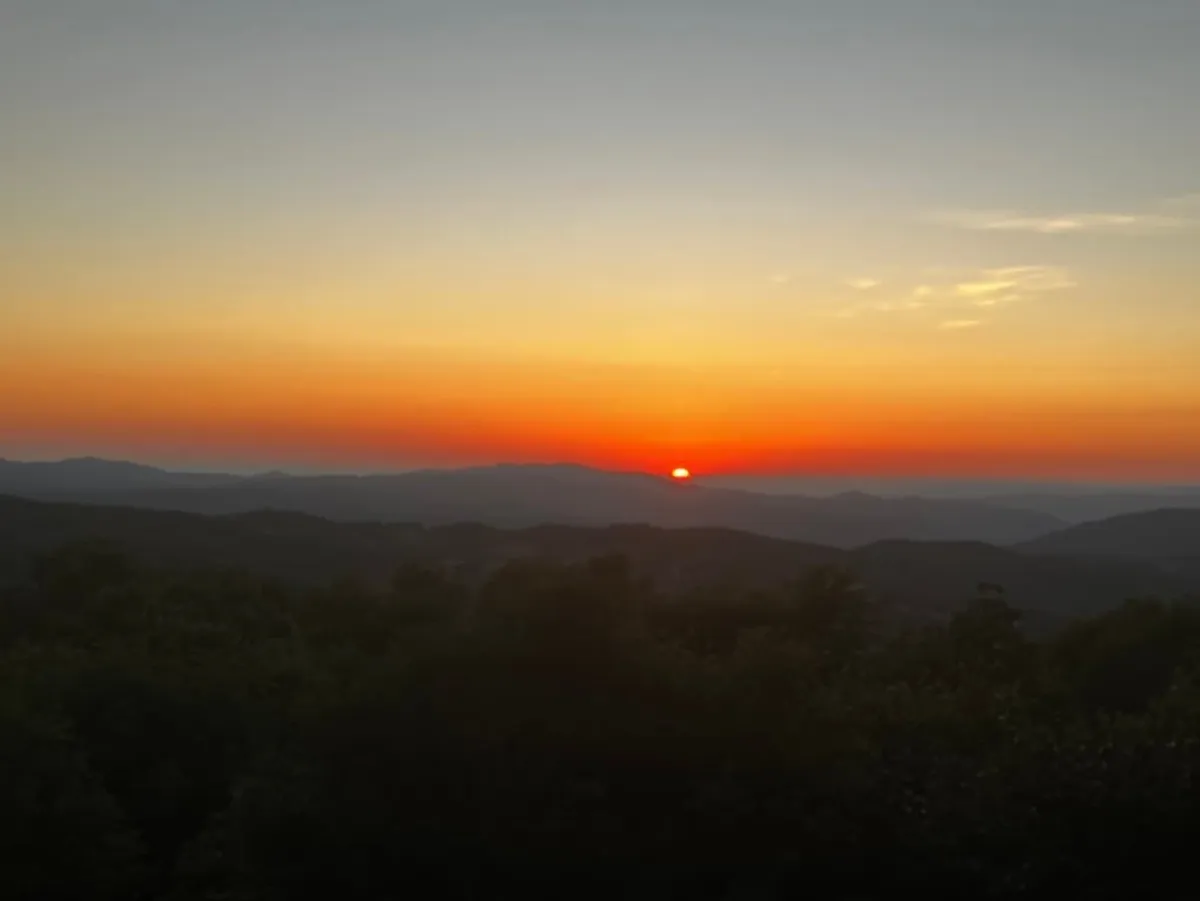 A breathtaking view of a sunset over a vast mountain range, with vivid sky colors blending into the landscape. This scene represents the multi-state views mentioned in the section and the unique mountain atmosphere that awaits guests and their dogs.