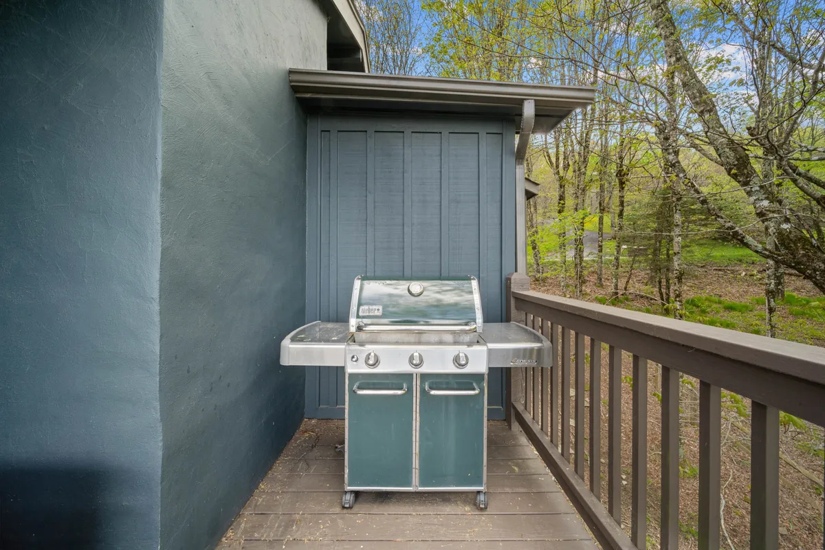A grill stands ready on a wooden railing with greenery in the background, hinting at communal outdoor meals and summer barbecues. The background scenery and setup evoke memorable gatherings with family and friends in a tranquil, natural setting.