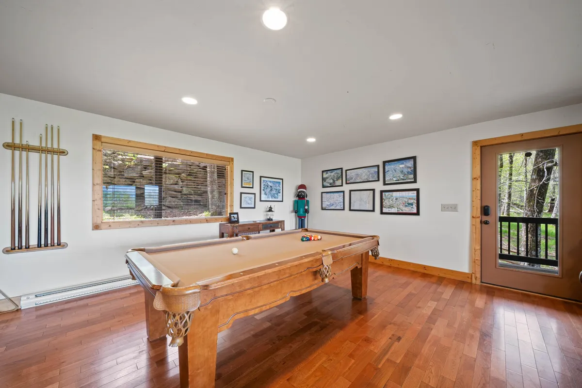 A playful, relaxed atmosphere is captured in this room featuring a pool table positioned by a large window, artwork on the walls, and a door leading directly outside. Natural light floods the space, reinforcing the connection to the outdoors.