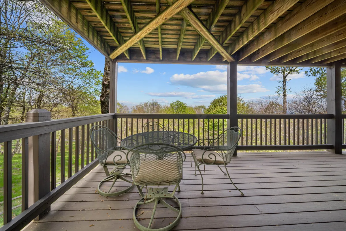 A serene exterior space featuring a covered outdoor seating area with expansive views of lush greenery and distant mountains. The wooden ceiling structure adds a rustic charm, perfect for enjoying nature at any time of day.