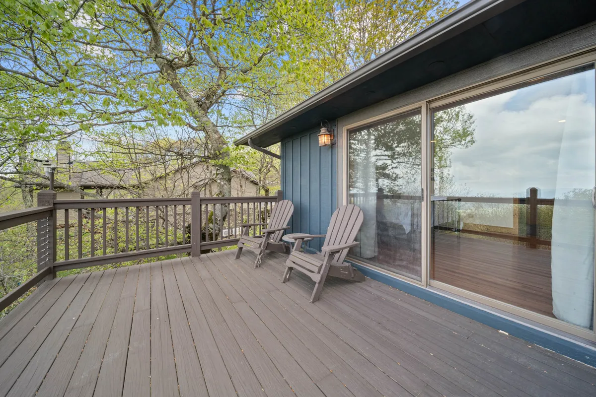 The image shows a serene wooden deck bordered by large windows, with comfortable deck chairs positioned to face the surrounding forest. Towering trees frame the space, making it an inviting spot for sunrises, stargazing, and soaking in the natural beauty after a day of exploring the region.