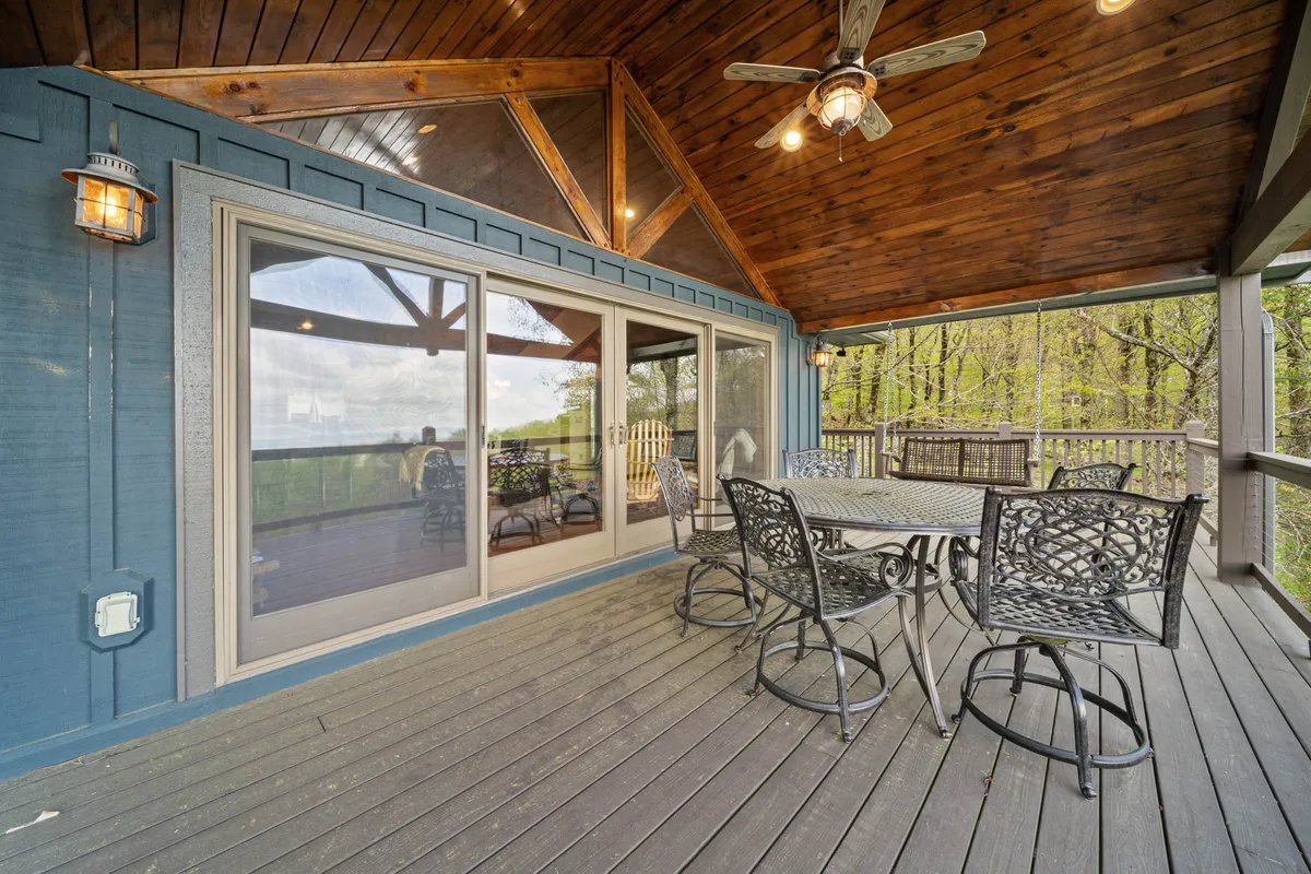 This image features a spacious upper deck equipped with a dining table and chairs beneath a wooden ceiling with beams. Large glass sliding doors provide seamless access to the indoors, and the elevated vantage shows off nature views and a sky that hints at sunset. The setup is ideal for outdoor family meals and gatherings, and the deck’s position suggests sweeping vistas—perfect for enjoying the four-state mountain panorama mentioned in the content.