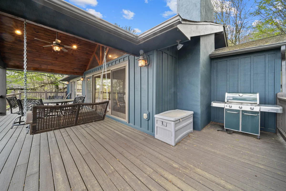 A spacious wooden deck complete with a comfortable outdoor seating area, a grill, and hanging light fixture, all framed by natural surroundings. The setup invites gatherings and meals in the open air.
