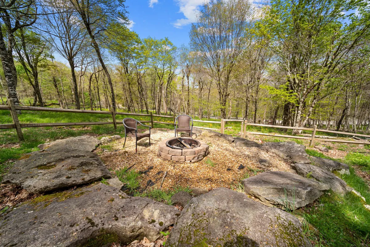A cozy fire pit area surrounded by natural rock seating and wooded surroundings. The scene is inviting and peaceful, ideal for evening gatherings, storytelling, or simply relaxing by the fire as the sun sets.