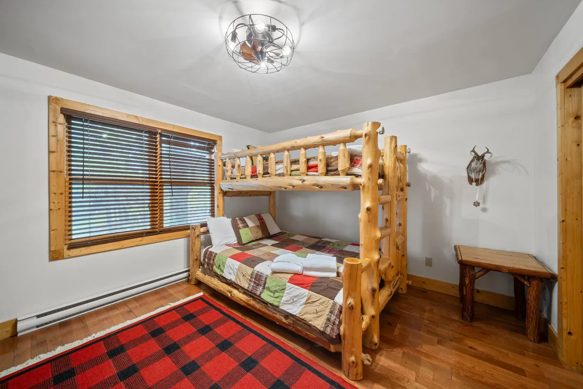 A cozy bunkroom featuring a sturdy wooden bunk bed with plaid bedding and accents. Warm lighting and wooden details create an inviting atmosphere ideal for children or friends.