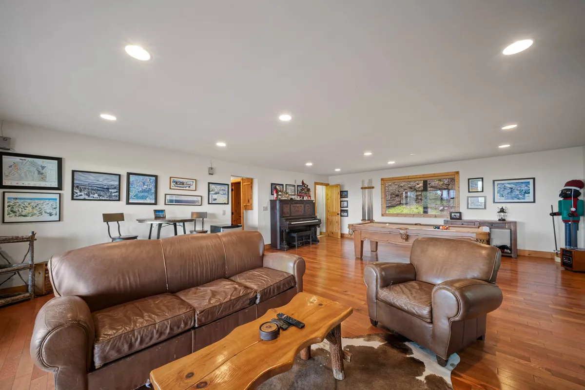 This photo centers on a comfortable, inviting game room setting featuring a leather sofa, wooden coffee table, pool table, and piano. The decor is warm, with artwork on the walls and an open layout that encourages both relaxation and activity.