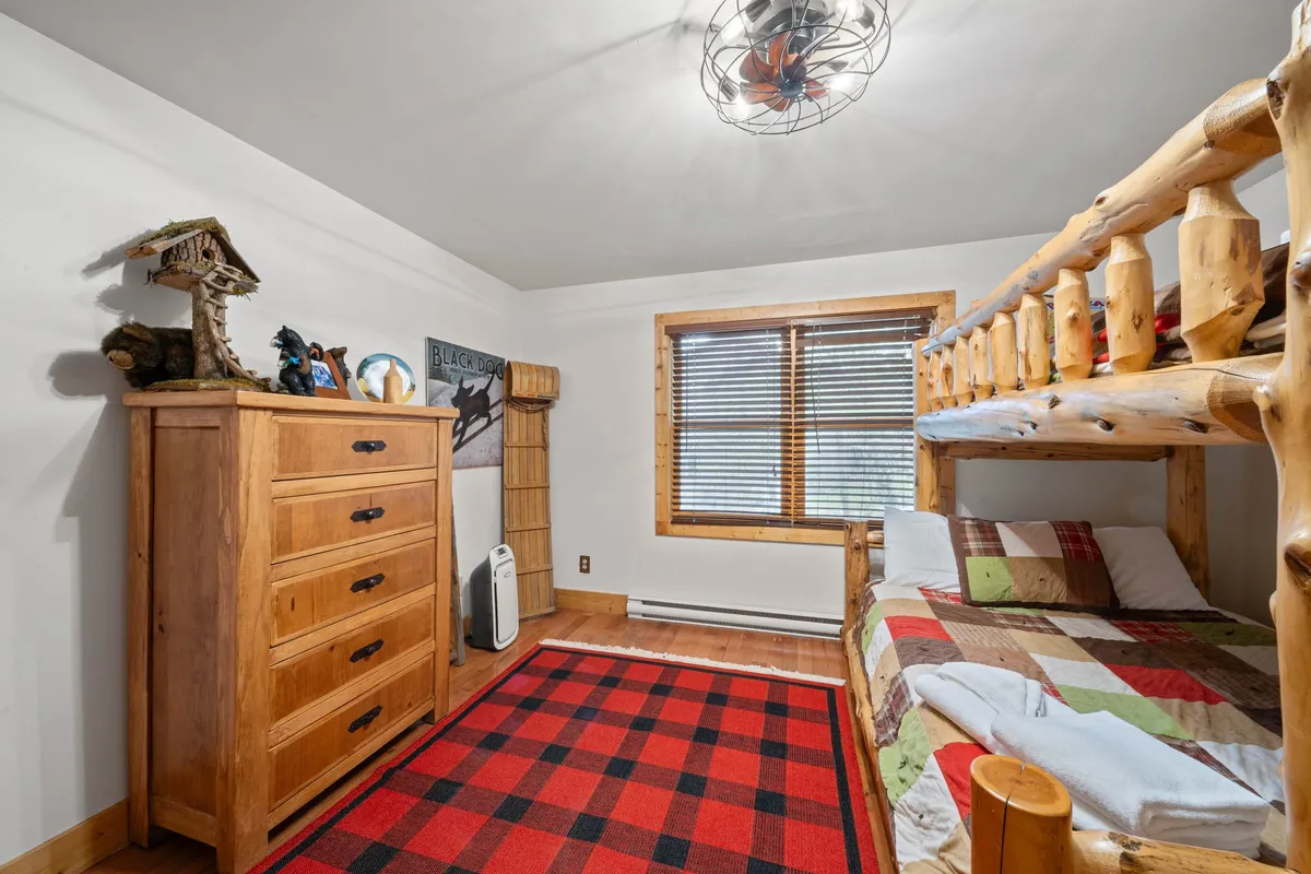 A cozy bunkroom with a wooden bunk bed, plaid rug, wooden dresser, and children’s artwork on the wall. The inviting space is clearly designed for younger guests, offering a playful and functional retreat for kids to sleep, read, and play.
