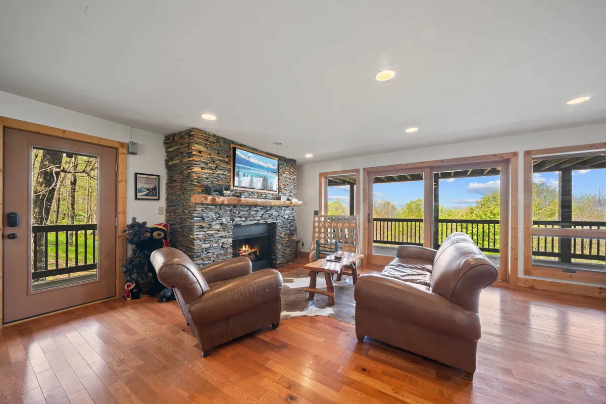 A spacious lower living area with a stone fireplace, large windows letting in natural light, and comfortable seating. The setup is perfect for relaxing, watching TV, or gathering around the warmth of the fire with family and friends.